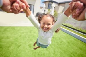 A happy young girl being spun by her parent outdoors, illustrating the emotional needs and stability that Ontario courts prioritize under the "best interests of the child" test when determining parenting arrangements.