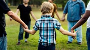 A young boy holding hands with adults in a circle in a grassy park, symbolizing family stability and the importance of calculating child support income in Ontario accurately.