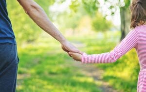 Parent holding hands with a young child outdoors, representing family law and changing a parenting order.
